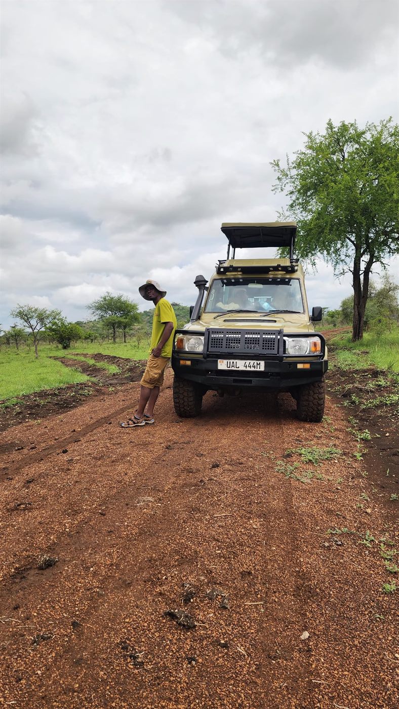 Paius beside a safari vehicle on a dirt road