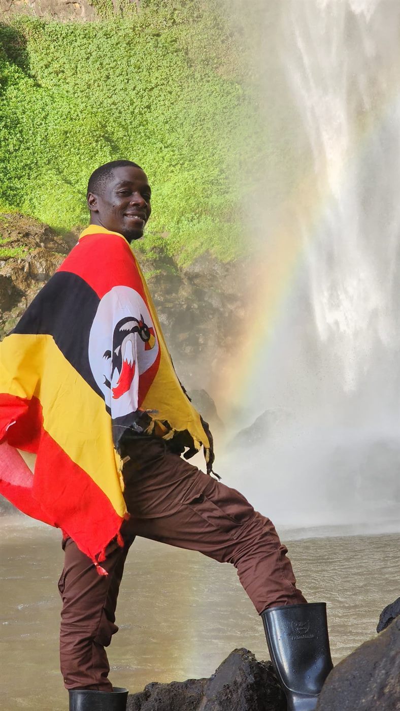 Paius wrapped in the Uganda flag near a waterfall
