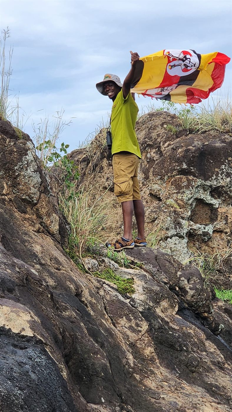 Paius waving the Uganda flag on rocks