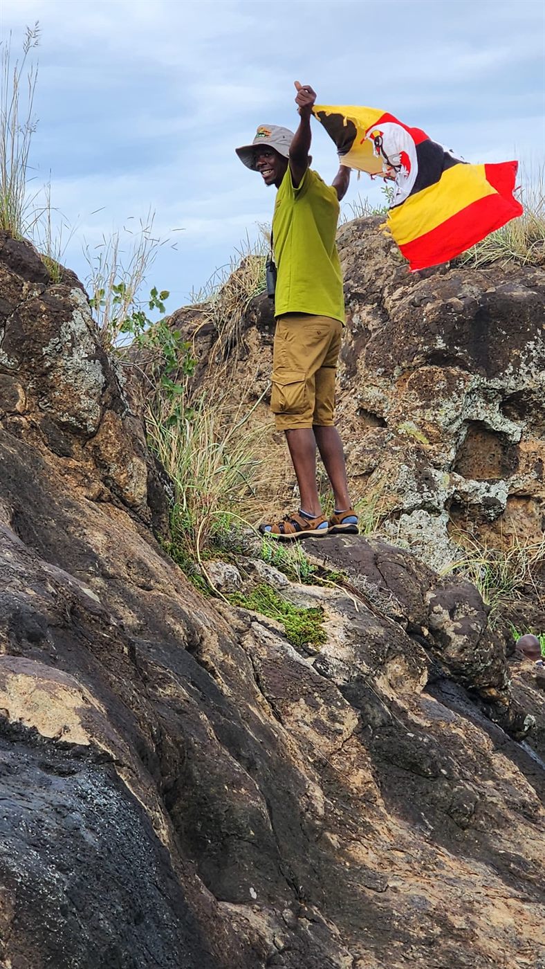 Paius holding a Uganda flag on rocky terrain